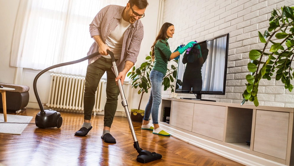 Ein Mann saugt beim Frühjahrsputz Staub, während eine Frau den Fernseher reinigt