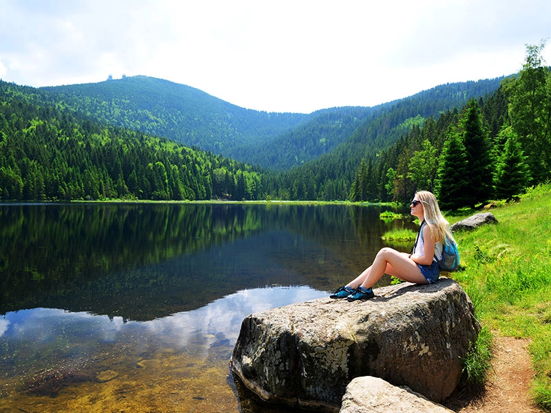 Ein Frau sitzt auf einem Felsen am See umgeben von Wald