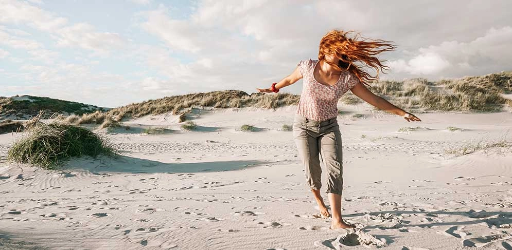 Junge Frau läuft mit ausgebreiteten Armen über einen Strand